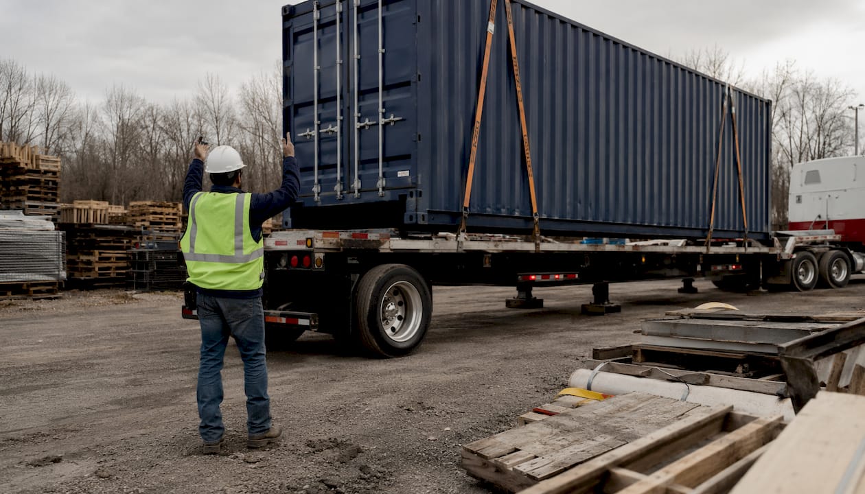 Worker directing container delivery truck onsite